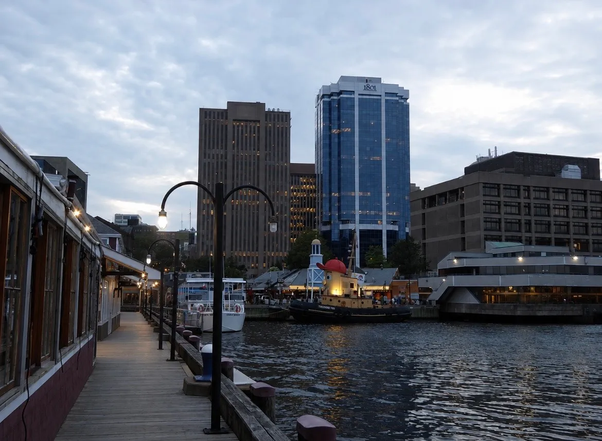 Halifax's waterfront boardwalk at dusk, with Theodore Too the tugboat moored below the towers.