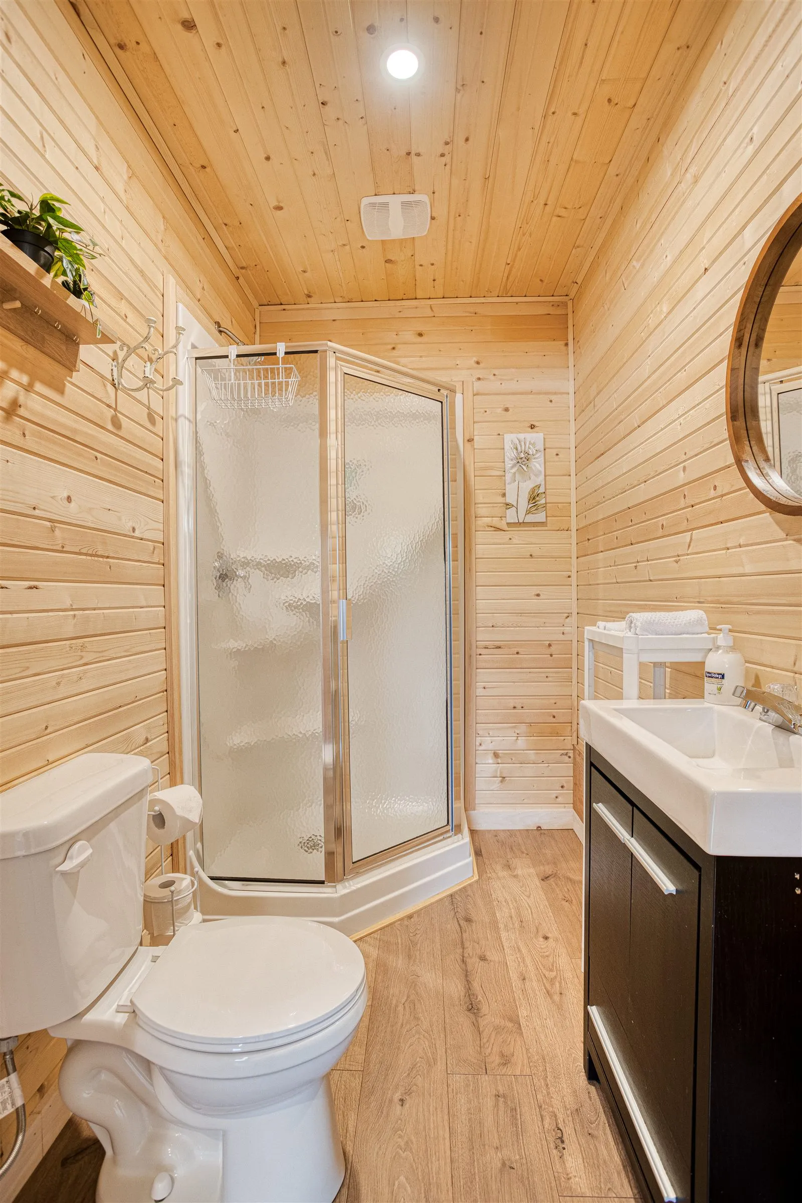 Bathroom with a corner glass shower, dark wood vanity, and warm pine walls.