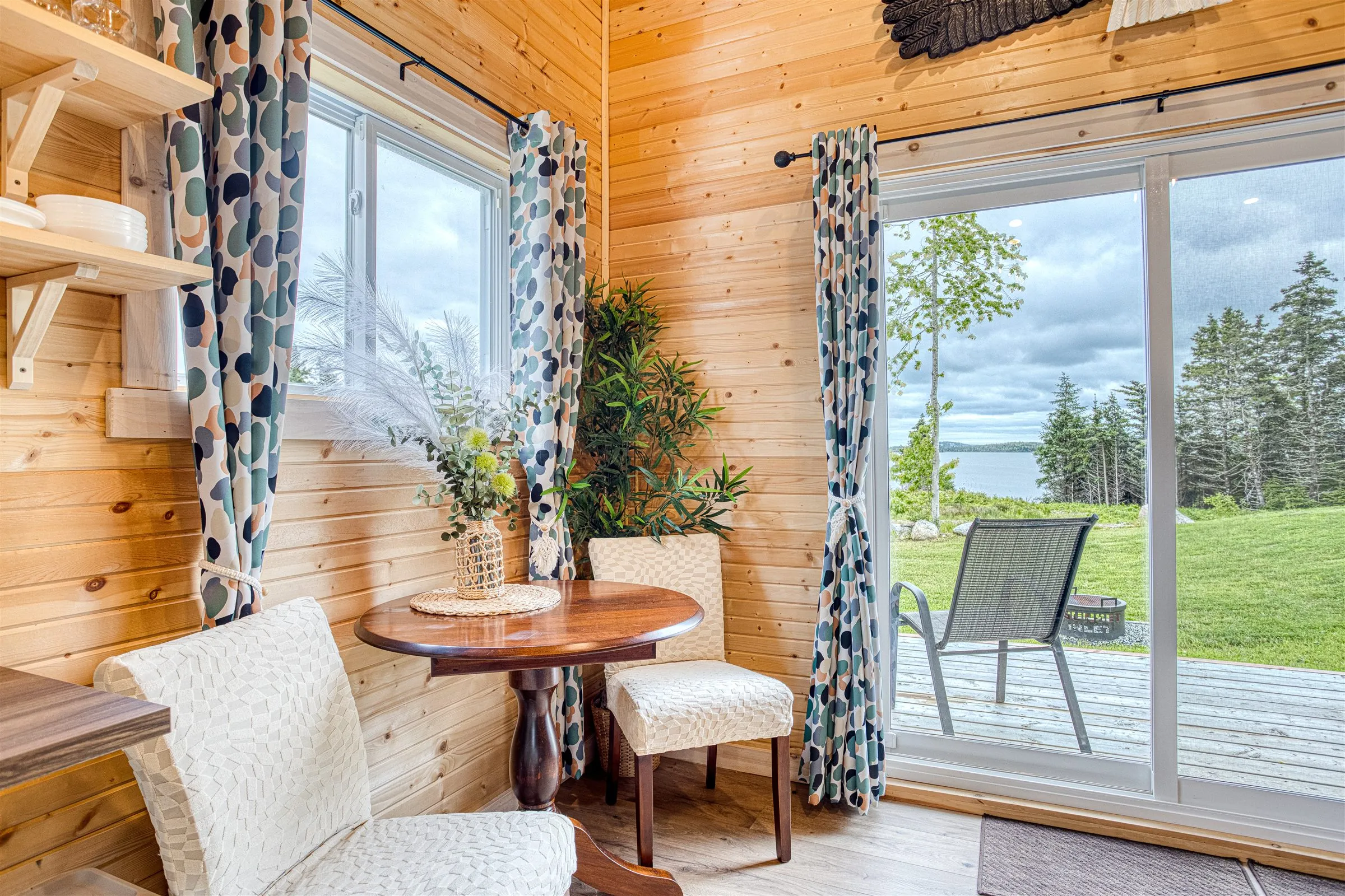 A round dining table beside sliding glass doors that look out over the lawn to the inlet.