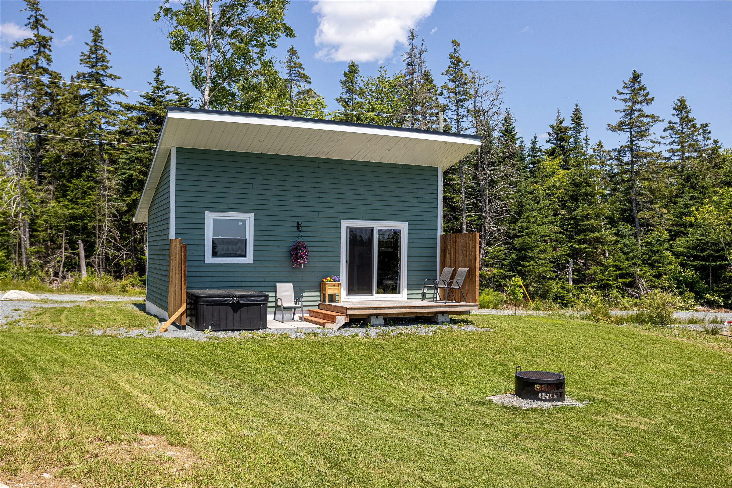 Helen's Haven, a teal cabin with a back deck, private hot tub, and fire pit on a sunny hilltop lawn.