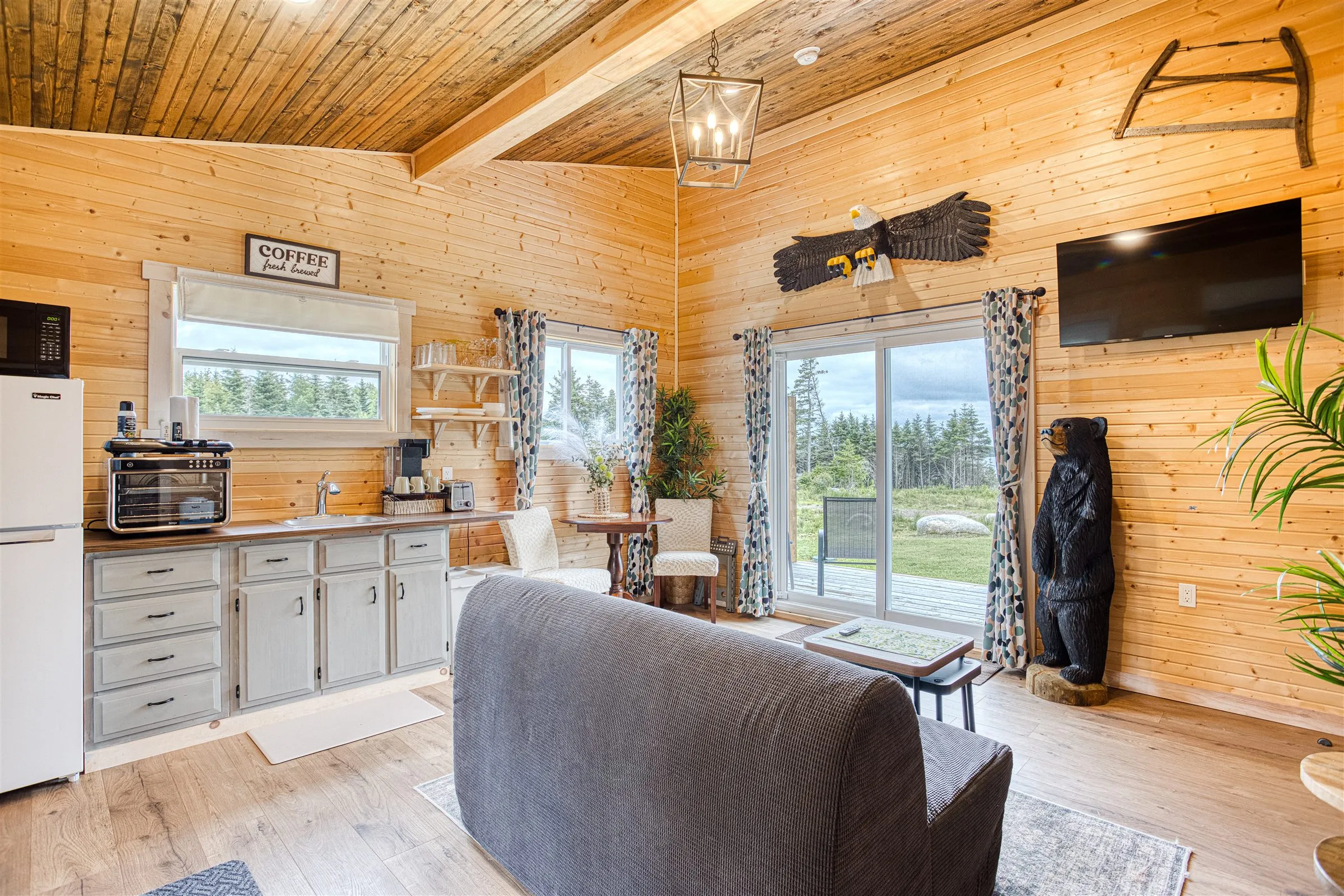 Open-plan interior with a kitchenette, coffee bar, and sofa beneath a vaulted wood ceiling.