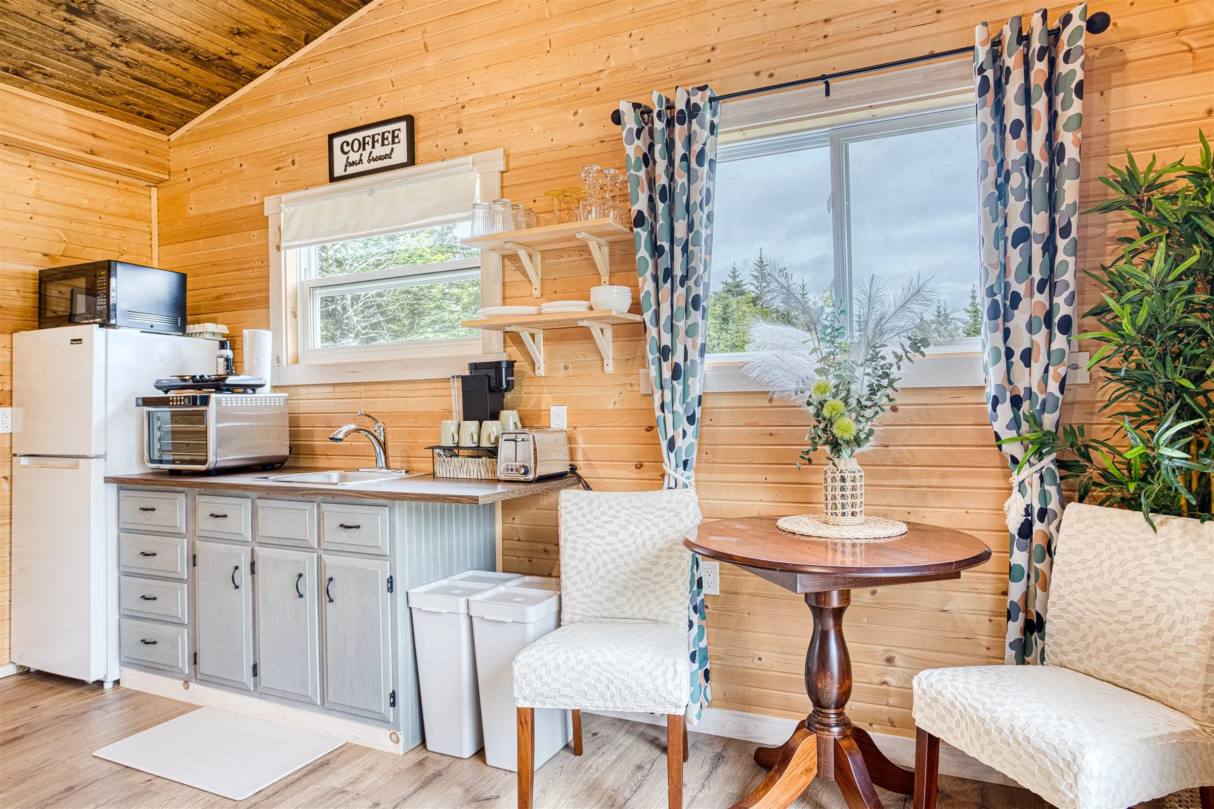 Compact kitchenette with grey cabinets and a coffee station beside the round dining table.