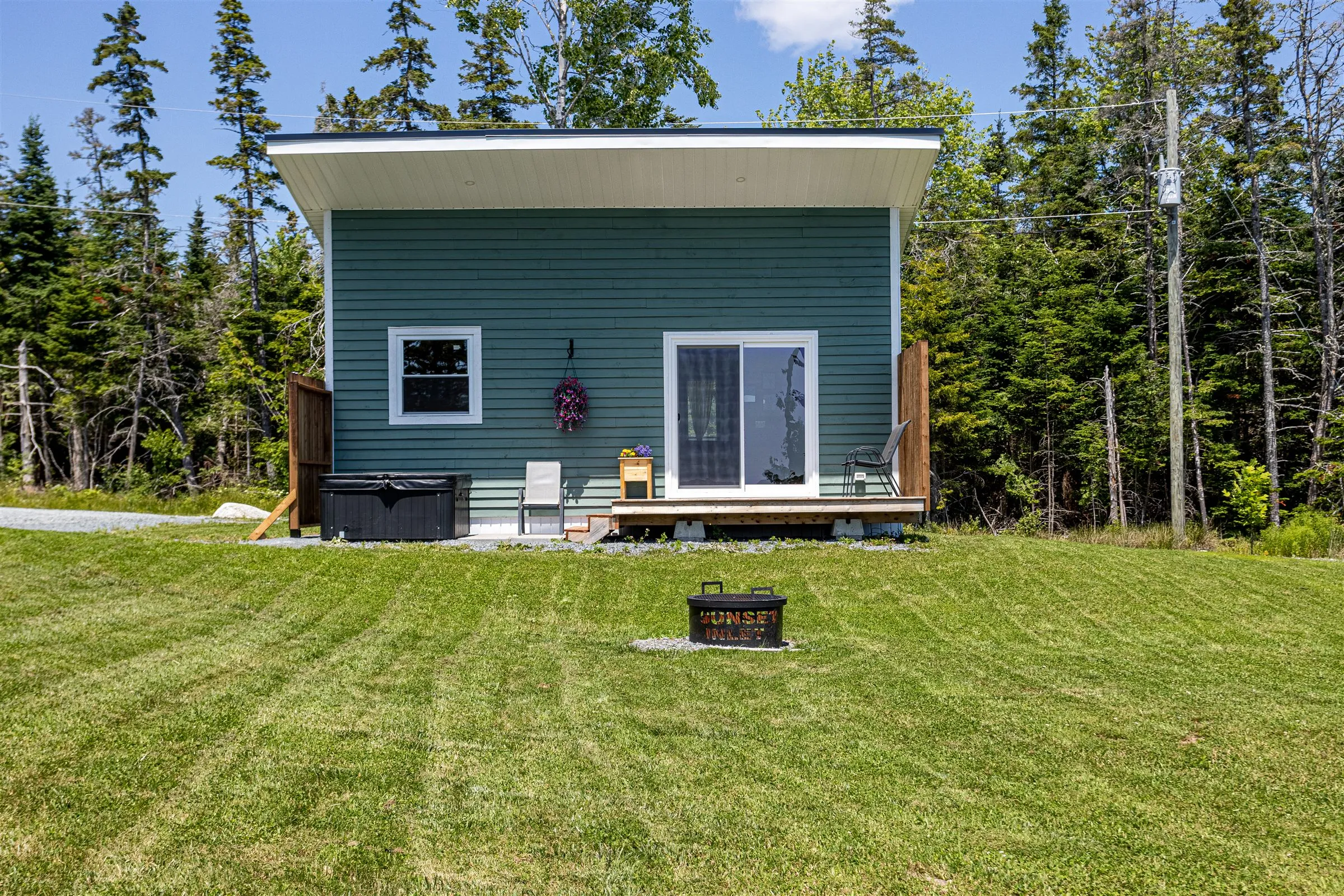 Back of the cabin with sliding glass doors and a Sunset Inlet fire pit waiting on the lawn.