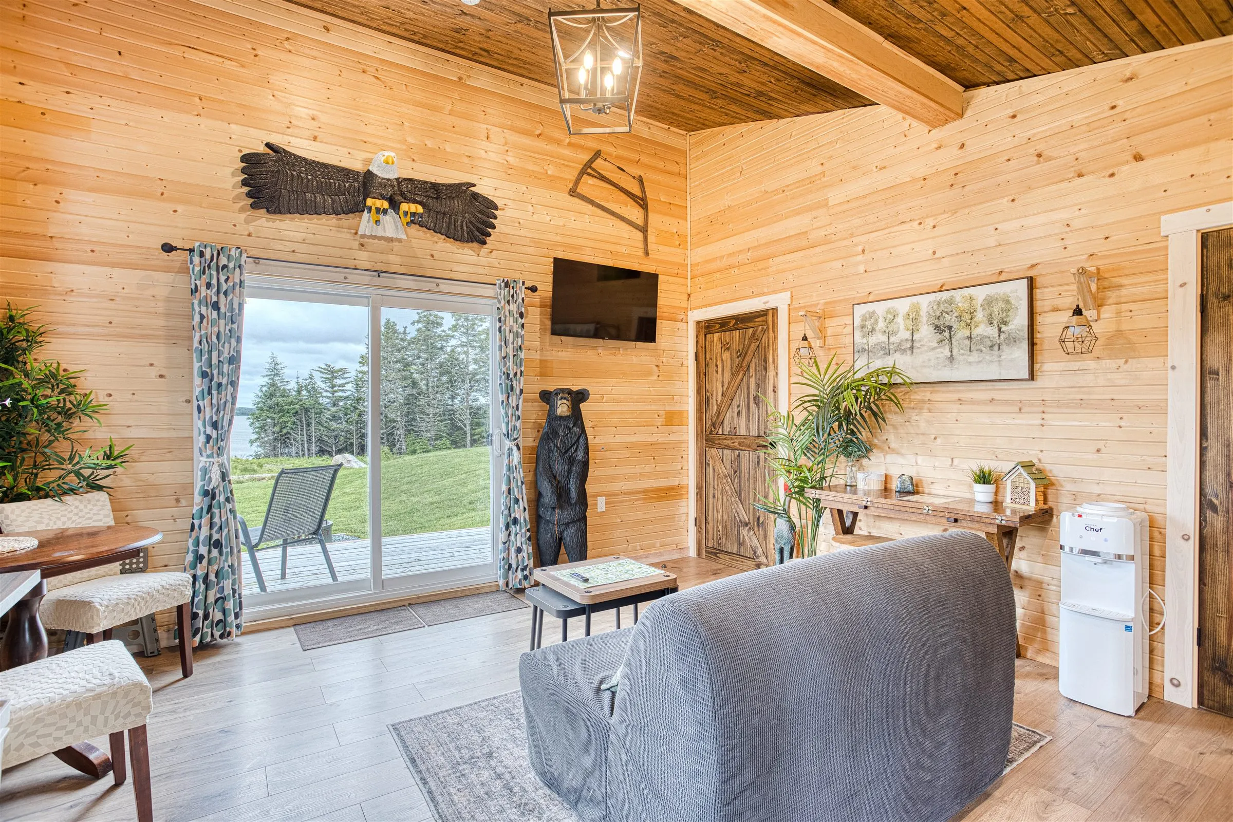 Pine-panelled living area with a grey sofa bed, wall-mounted TV, and sliding doors to the lawn.