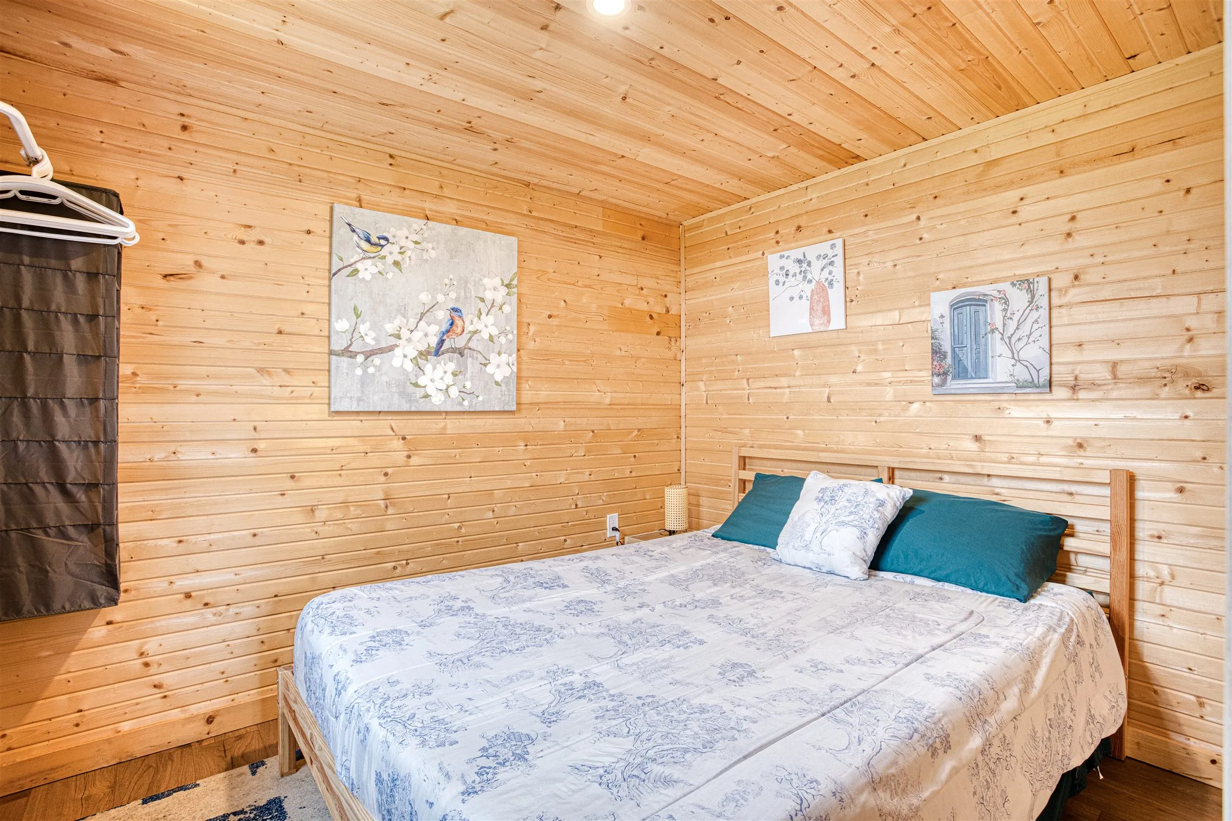 The bedroom with a wood-slat headboard, floral bedding, and knotty pine walls.