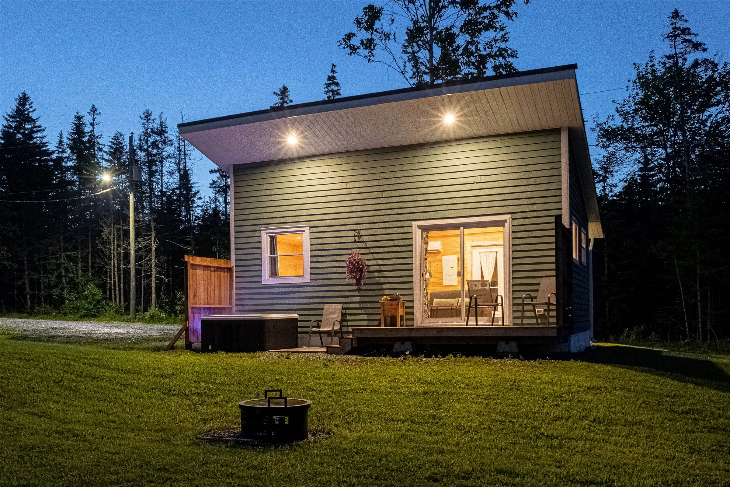 Helen's Haven glowing warmly at twilight, with the hot tub and fire pit in the foreground.