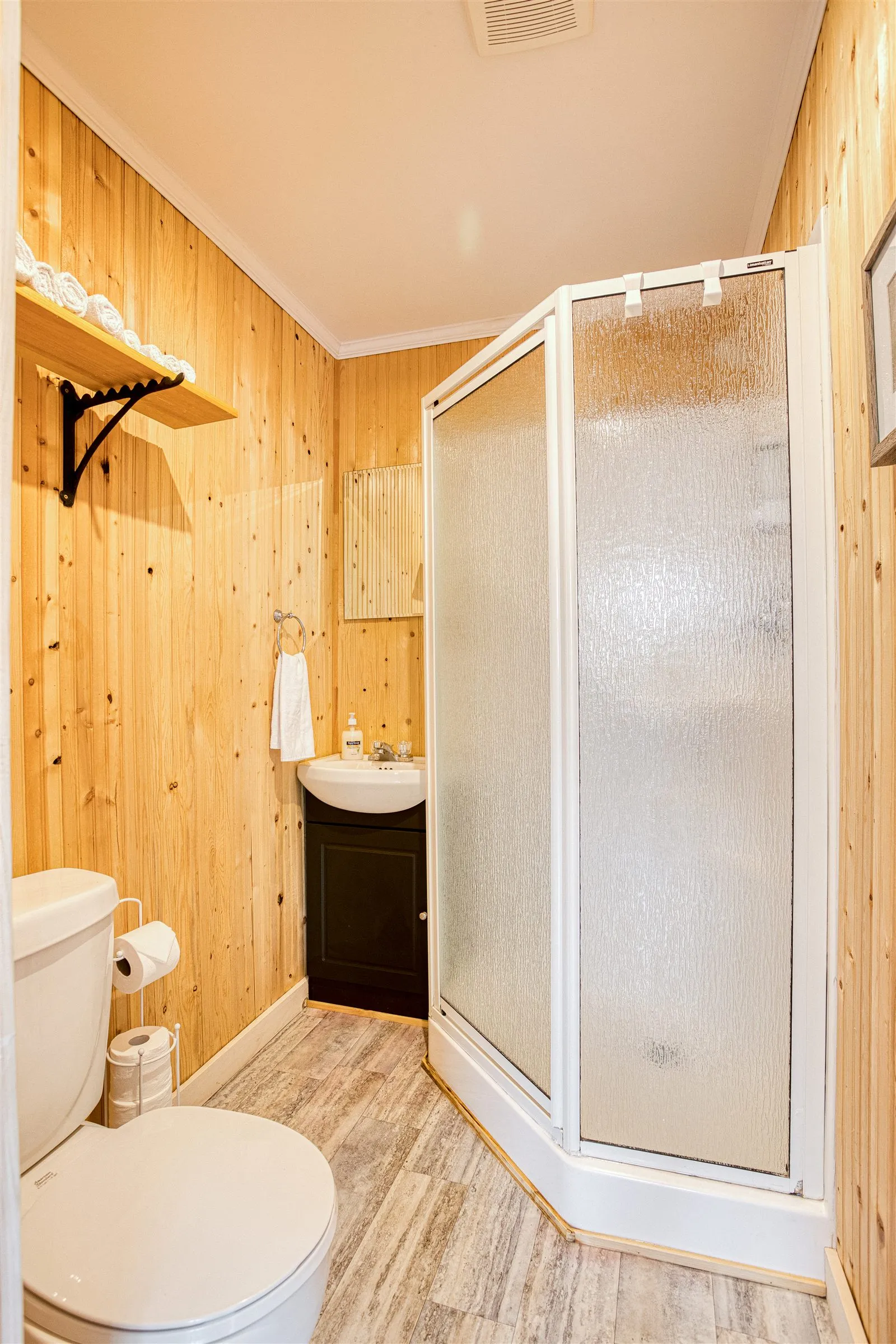 Cabin bathroom with corner glass shower, vanity, and fresh towels.