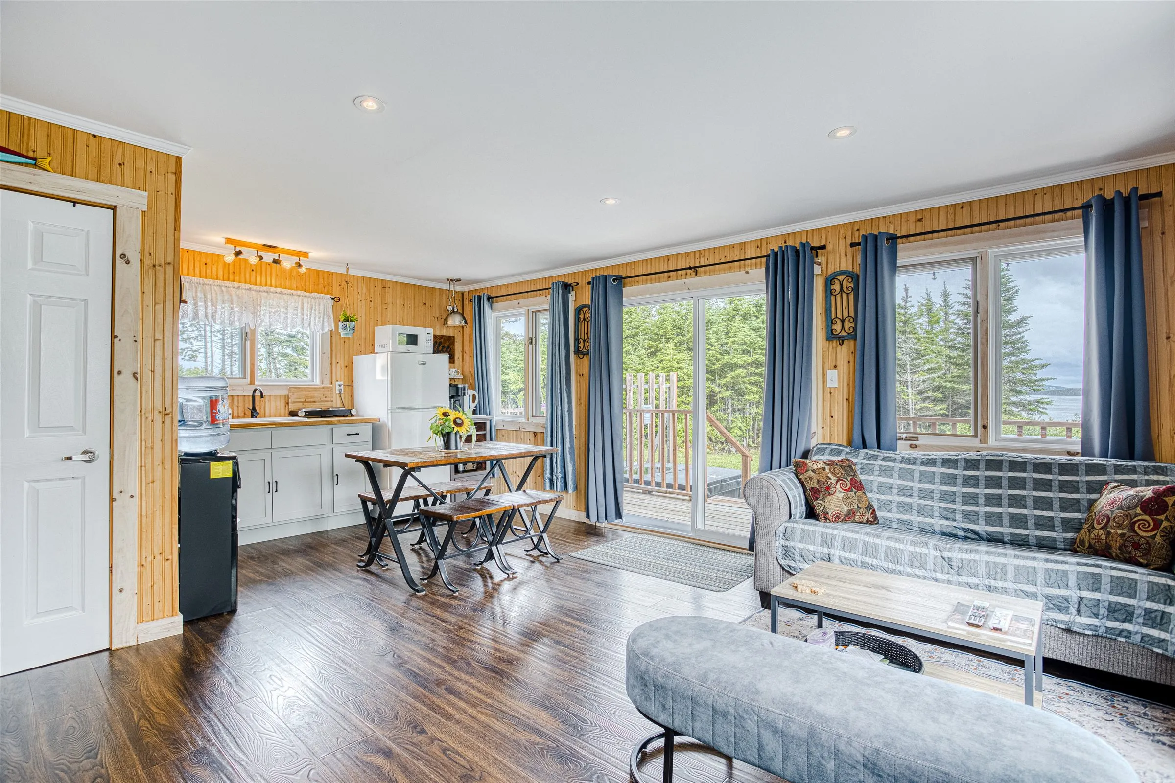 Open-plan living area with kitchenette, dining table, and sofa in warm pine panelling.