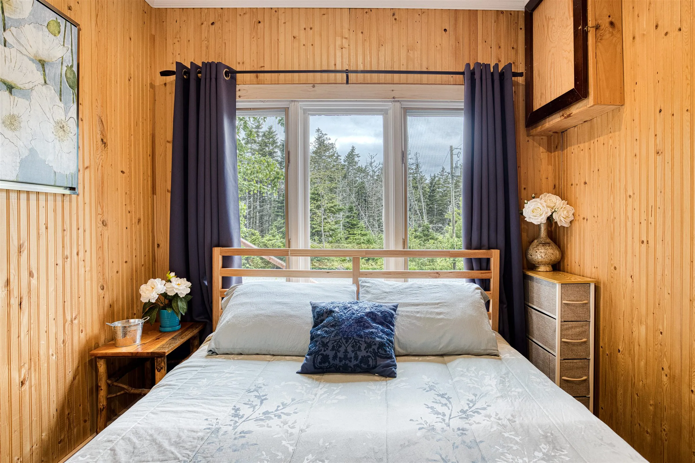 Queen bedroom with a wooden bed frame beneath a large forest-view window.