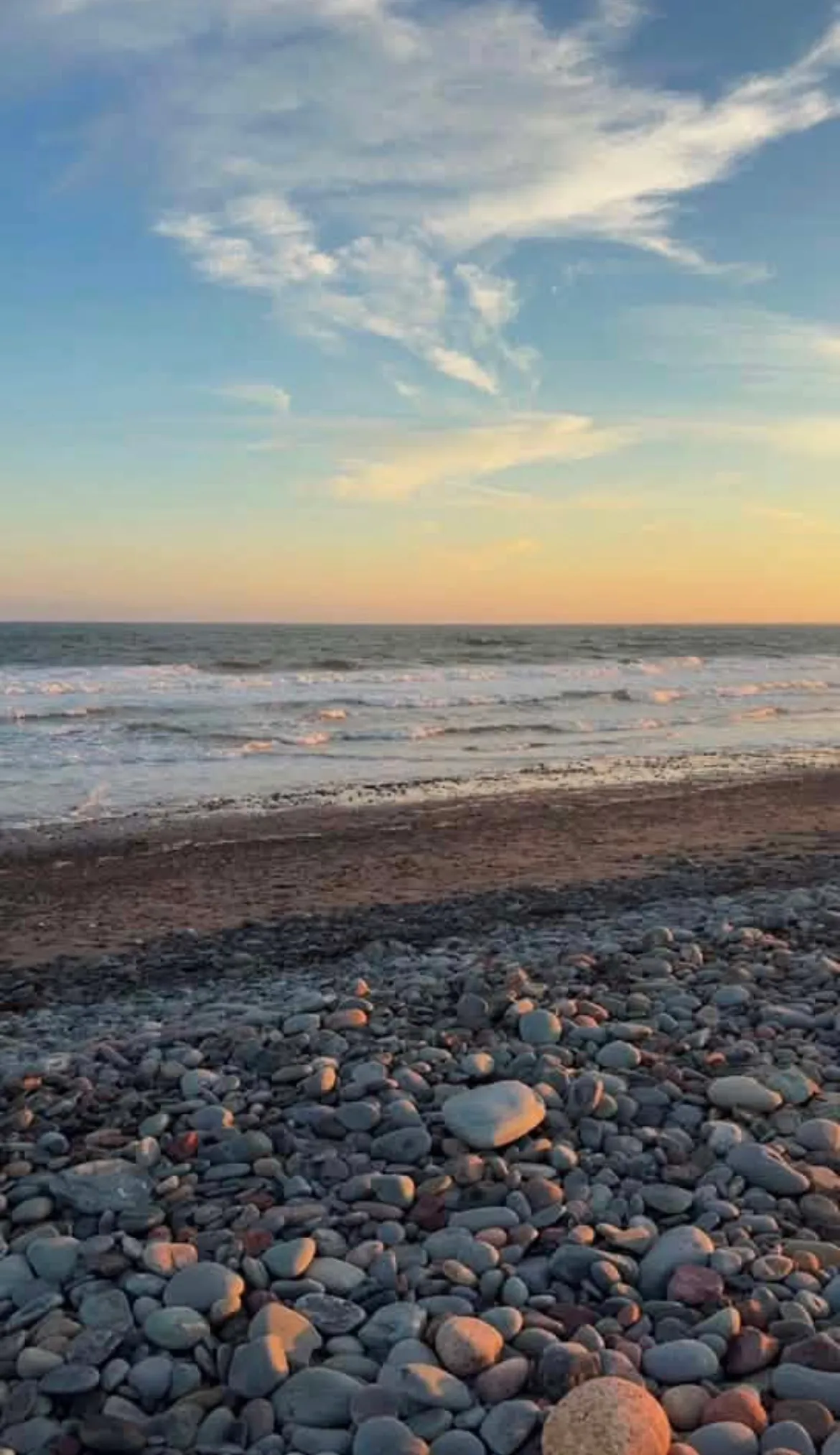Waves rolling onto the cobblestone shore of Lawrencetown Beach at sunset.