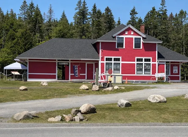 A red heritage station building with an Open banner, backed by evergreens in Musquodoboit Harbour.