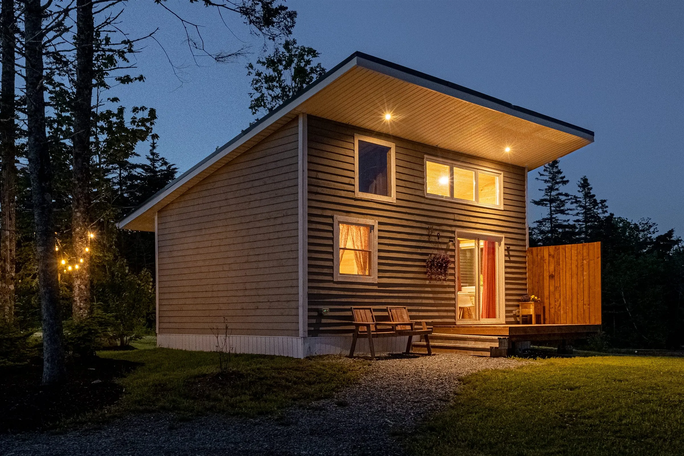 Norma's Retreat glowing with warm window light at dusk, string lights in the trees beside the deck.