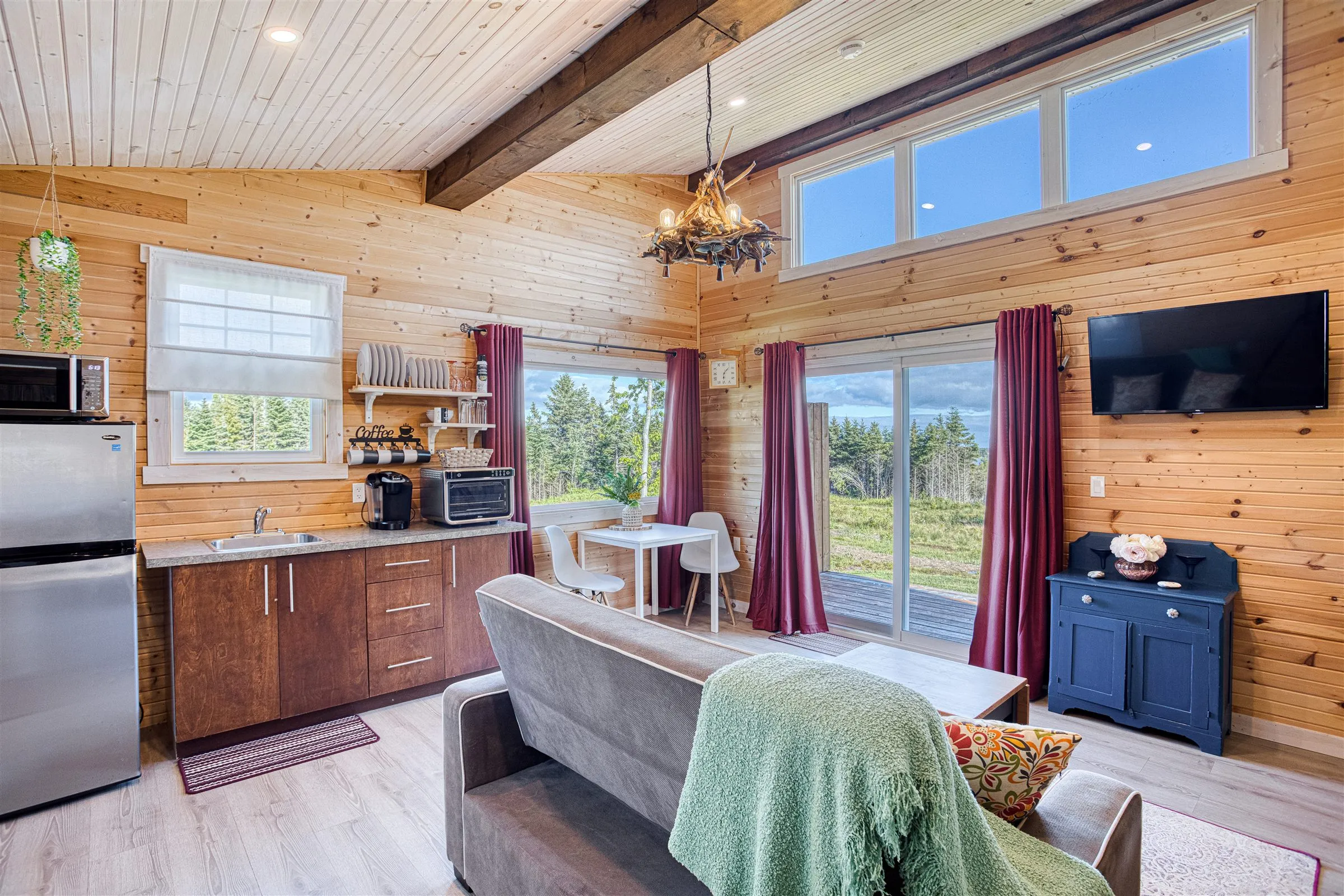 Open-plan living area with pine walls, kitchenette, grey sofa, and clerestory windows.