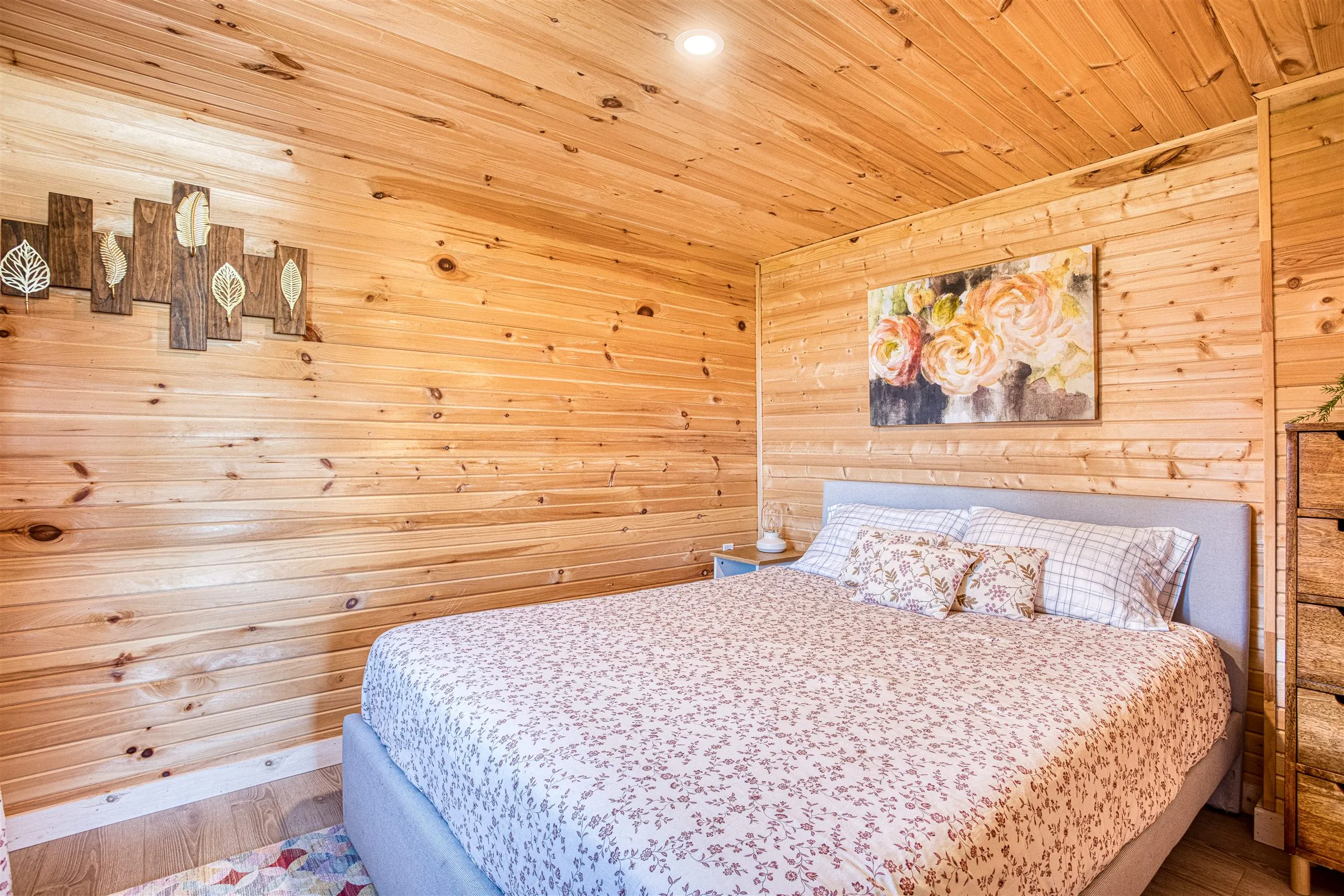 Cozy pine-panelled bedroom with an upholstered bed and floral quilt.