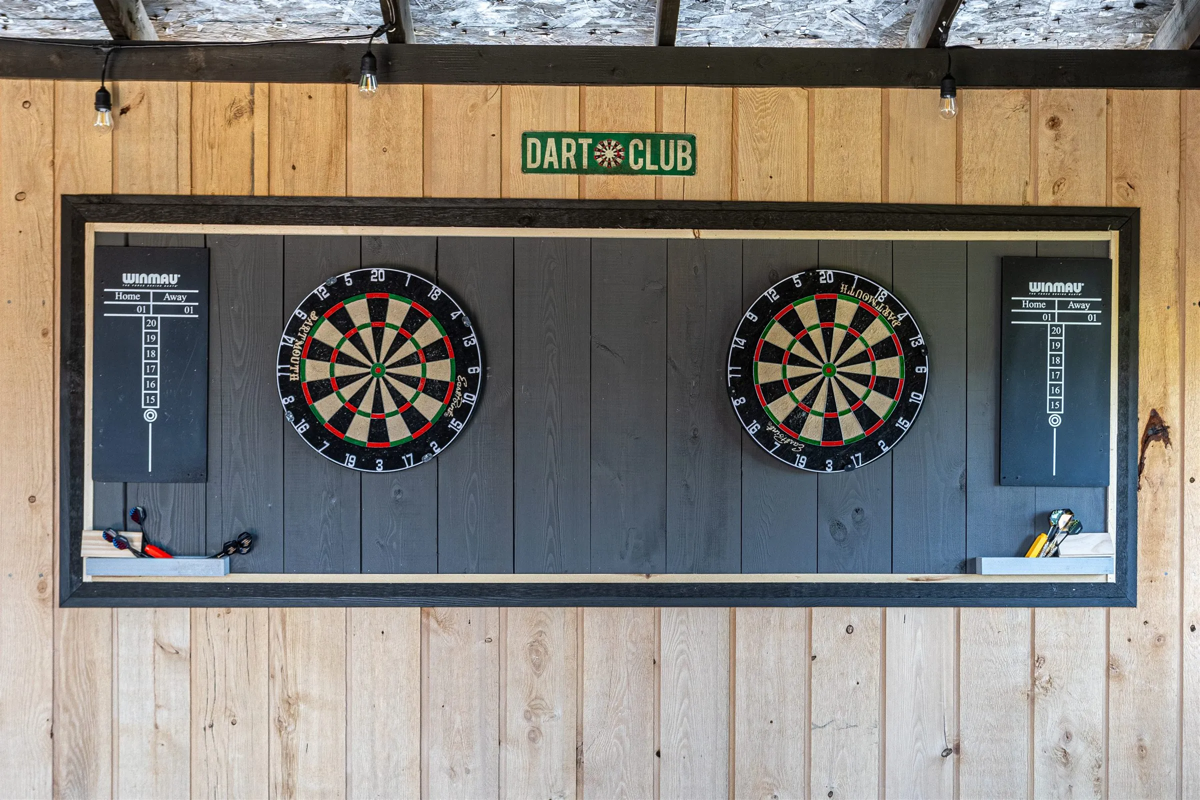The Dart Club sign hangs over twin dartboards and chalk scoreboards.