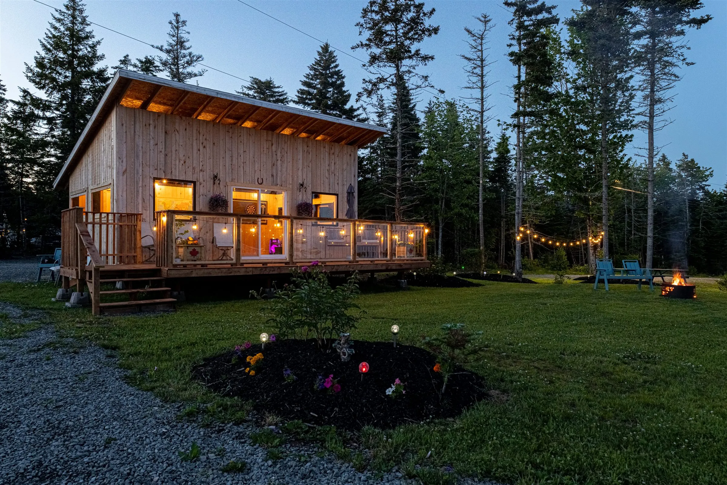 The clubhouse lit up at dusk with string lights on the deck and a campfire burning nearby.