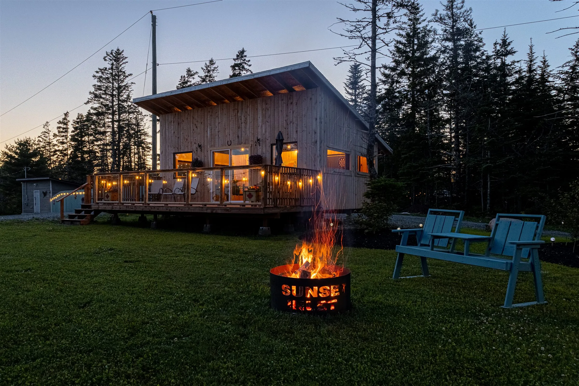 Flames rise from the fire pit on the lawn as the clubhouse deck glows at dusk.