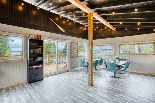 Inside the clubhouse - string-lit timber beams over shared tables, with the deck and inlet through the sliding door.