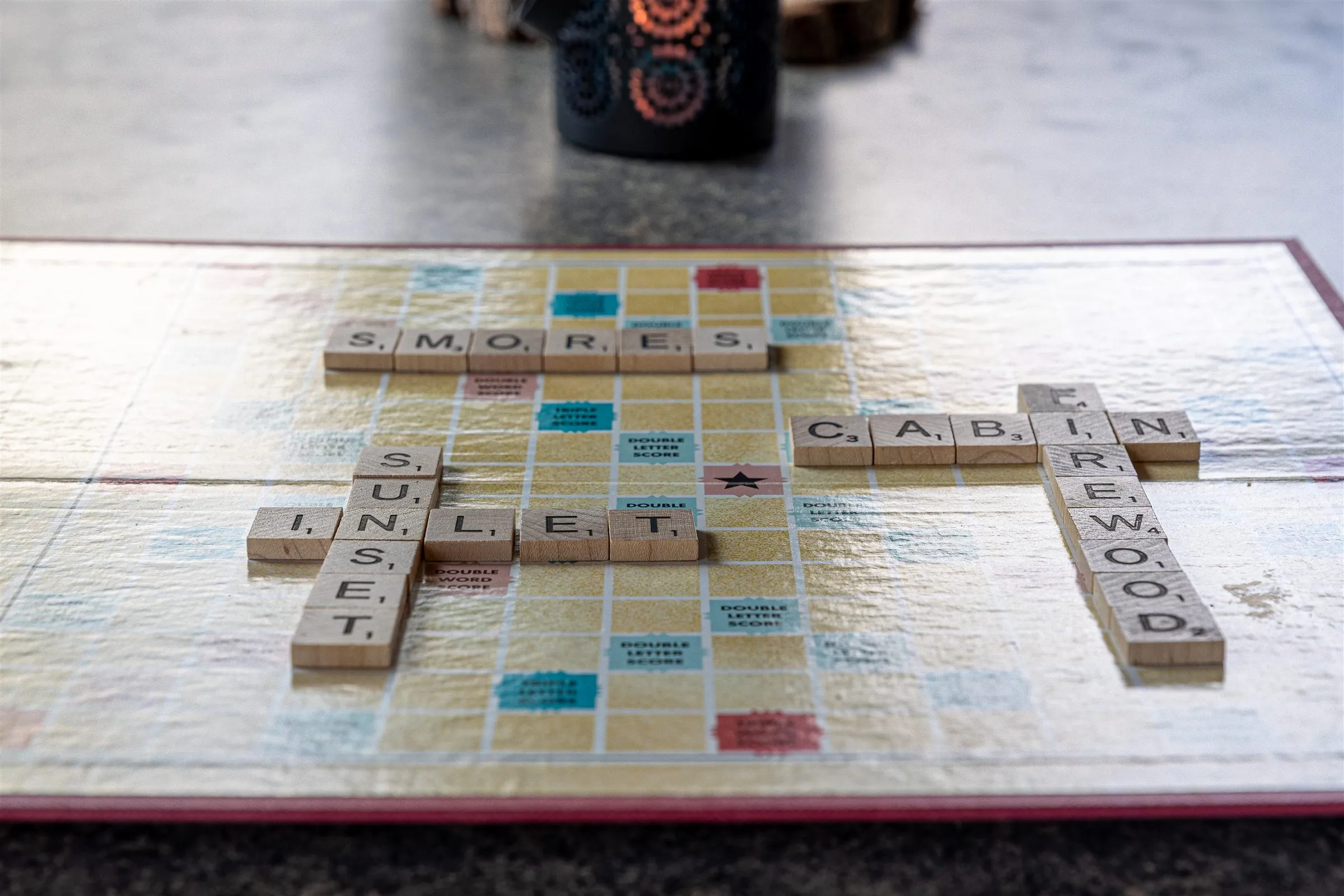 Scrabble tiles spelling s'mores, sunset, inlet, cabin and firewood.