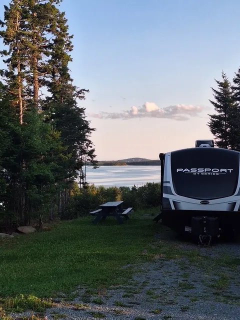 A fifth-wheel camper parked at Site 01 with a picnic table and the inlet view behind.