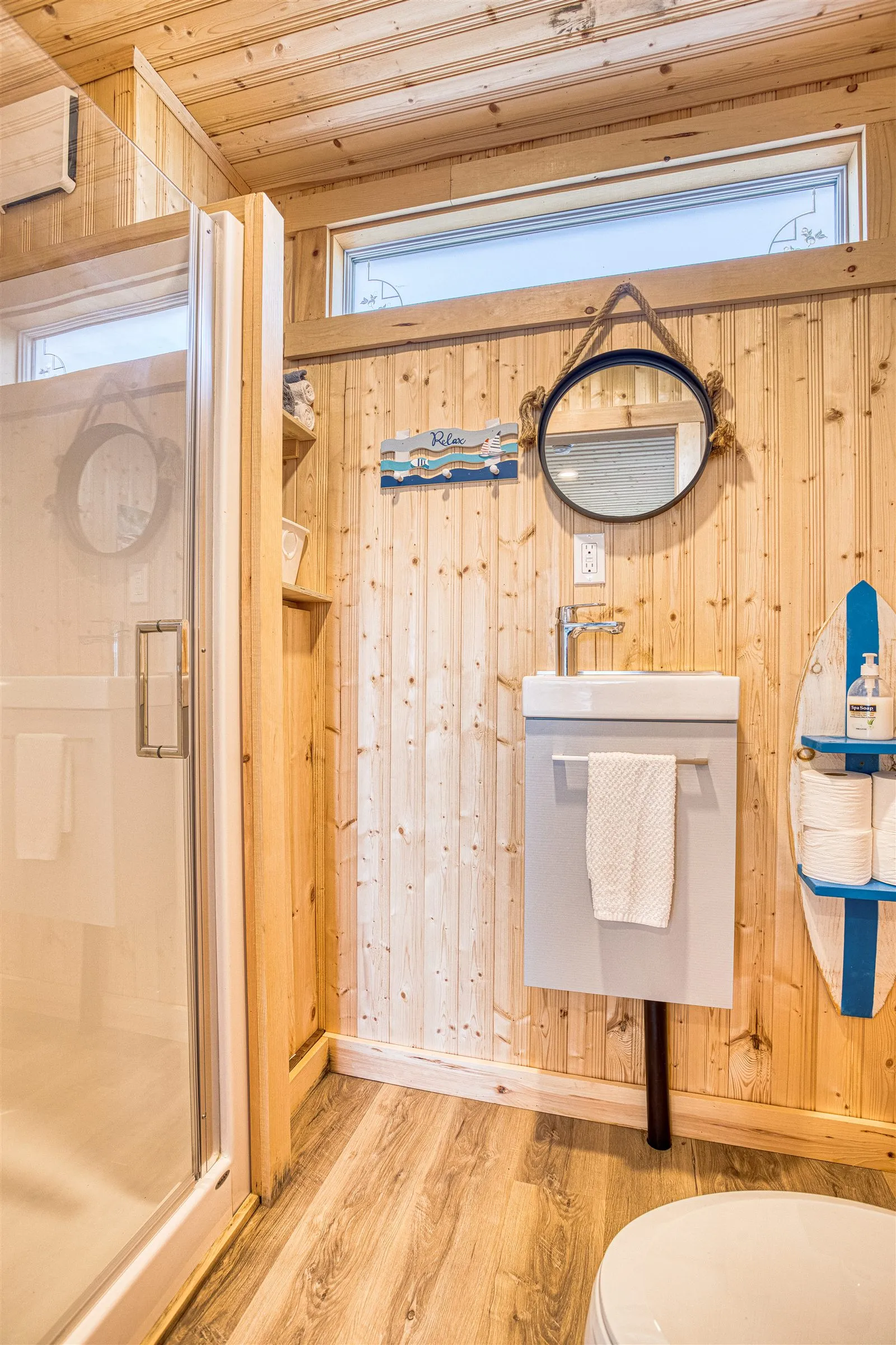 The bathroom with a glass shower, floating vanity, rope-hung mirror, and surfboard-shaped towel shelf.