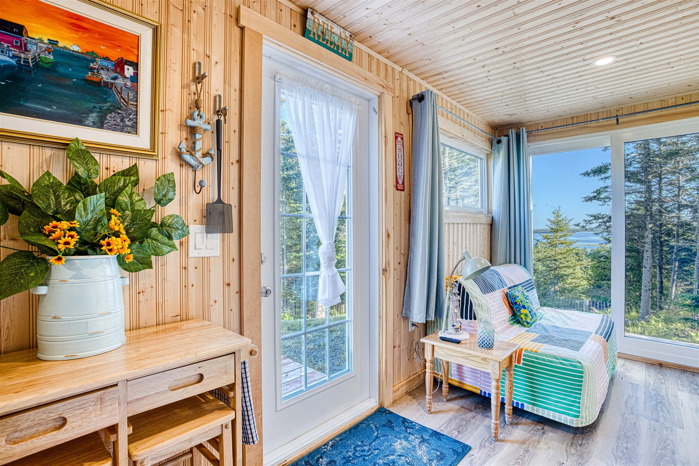 A daybed with a colourful striped quilt beneath windows framing trees and a slice of the inlet.