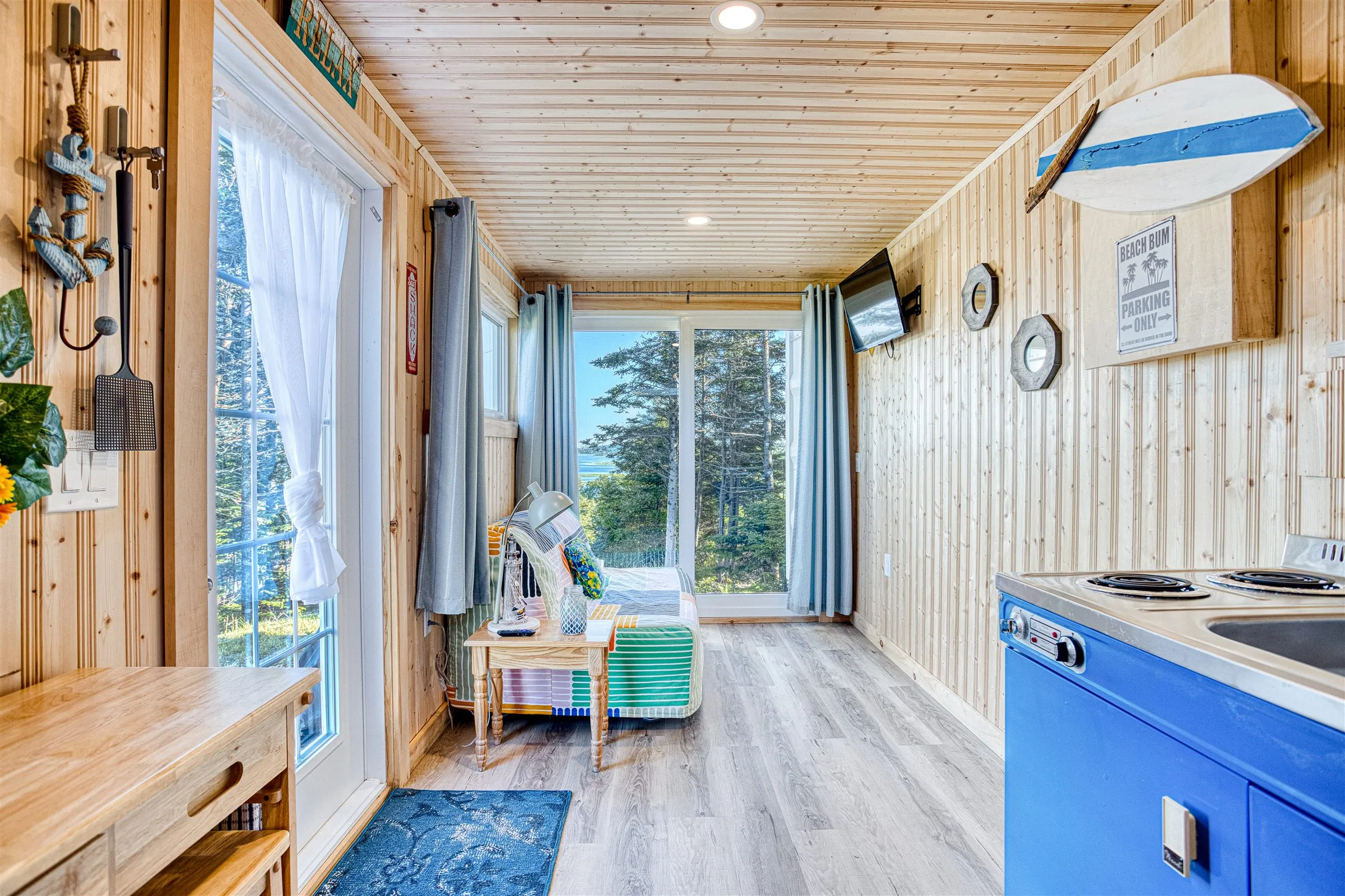 The long studio interior with a surfboard mounted above the blue kitchenette and a daybed by the window.