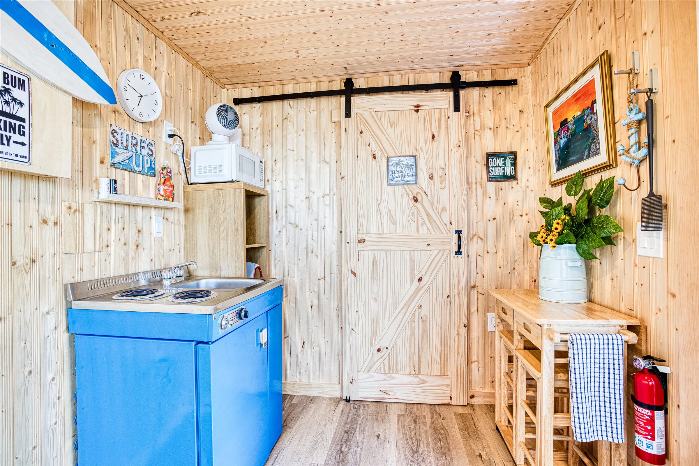 The compact blue kitchenette with two-burner cooktop and microwave beside a sliding pine barn door.