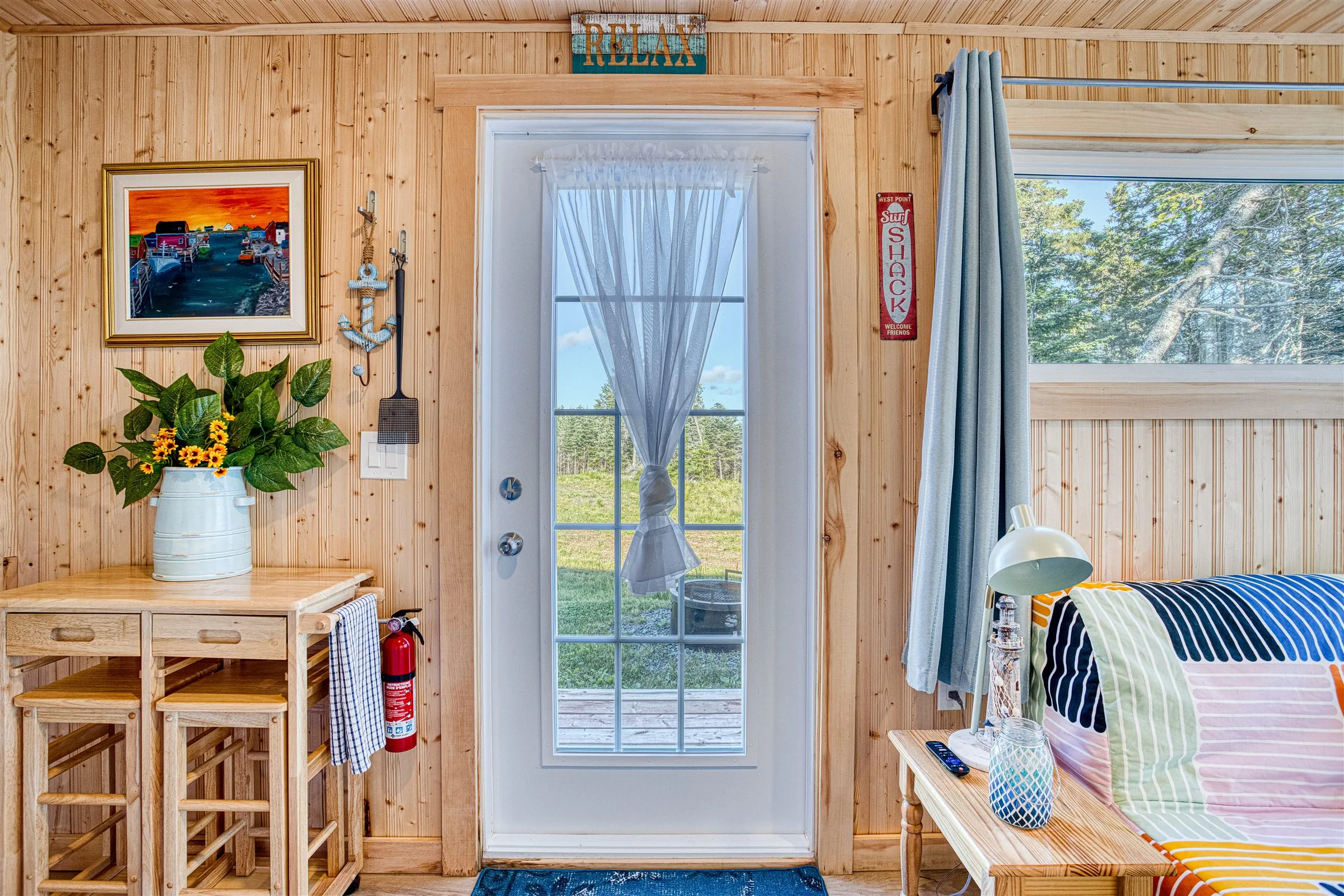 Knotty-pine interior with a curtained glass door, red Surf Shack sign, and sunflowers on the kitchen cart.